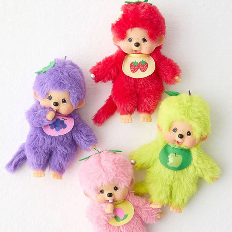 A set of four Monchhichi-style doll plushies. The top doll is strawberry red, the middle-left is grape purple, the middle-right is apple green, and the bottom is peach pink. Each doll has a tan plastic face, brown eyes, freckles, and is sucking its thumb or finger. They all wear a small bib and have a long, thin tail.