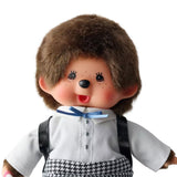 An officially licensed Monchhichi plush doll dressed in a school uniform with houndstooth pants and wearing a black patent leather backpack on its back