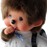 An officially licensed Monchhichi plush doll dressed in a school uniform with houndstooth pants and wearing a black patent leather backpack on its back