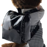 An officially licensed Monchhichi plush doll dressed in a school uniform with houndstooth pants and wearing a black patent leather backpack on its back