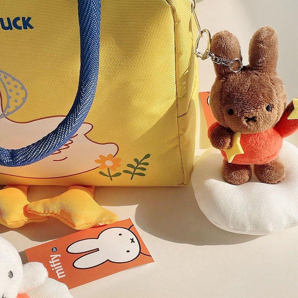 Official Miffy Melanie Dream Mascot Plush Keychains displayed with a yellow tote bag; featuring brown Melanie in orange outfits holding stars, a nostalgic minimalist Zen bag charm set for adult friendship gifts and office-core aesthetics. **perfect Easter basket stuffer for adults**; a minimalist Zen rabbit toy for **Easter Sunday home decor** and nostalgic spring gifting.