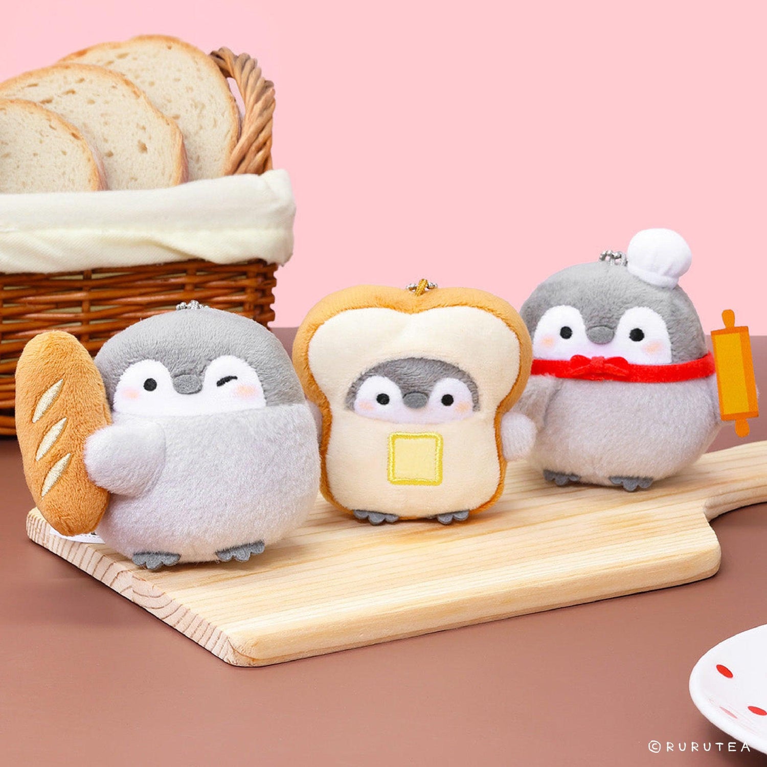 Official Spiralcute Koupen Chan Bakery Series Plush Mascot Keychain Collection featuring a winking penguin holding a baguette, a penguin inside a buttered toast costume, and a chef penguin with a rolling pin, displayed on a wooden cutting board with a silver ball chain to serve as a comforting workplace healing companion and emotional support tool for adult kidult collectors.