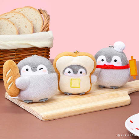 Official Spiralcute Koupen Chan Bakery Series Plush Mascot Keychain Collection featuring a winking penguin holding a baguette, a penguin inside a buttered toast costume, and a chef penguin with a rolling pin, displayed on a wooden cutting board with a silver ball chain to serve as a comforting workplace healing companion and emotional support tool for adult kidult collectors.