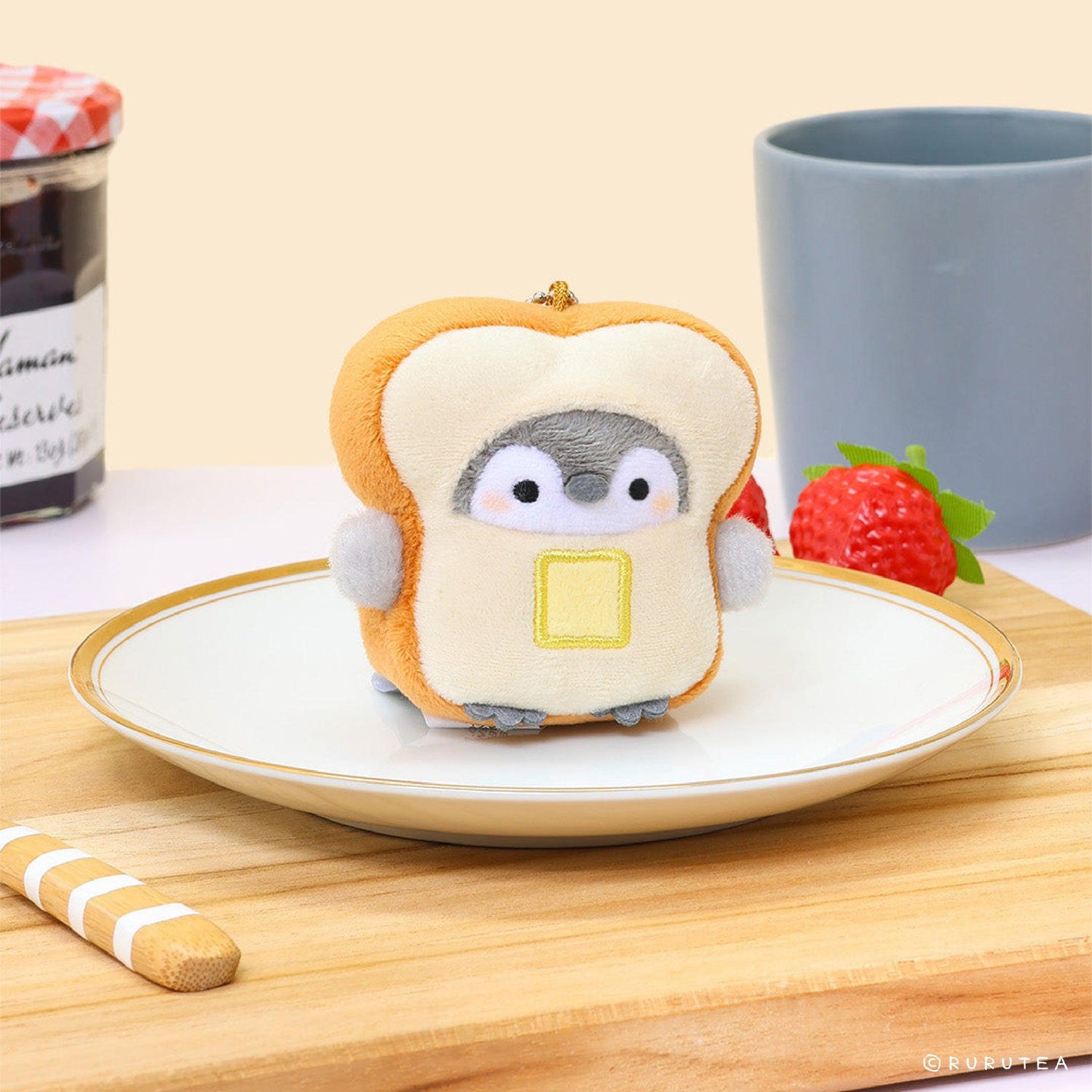 Officially licensed Spiralcute Koupen Chan Baker Costume Plush Mascot Keychain featuring a soft grey penguin embedded in a soft slice of bread with a yellow butter square detail, placed with strawberry and jam jar on a plate.