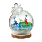 Officially licensed Re-Ment Pikmin Terrarium Collection Figure featuring one Red Pikmin on a giant green water lily pad and two Blue Pikmin in the clear 'water' base. All are enclosed in a round clear glass globe with a water drop design stopper, placed on a wood slice base.