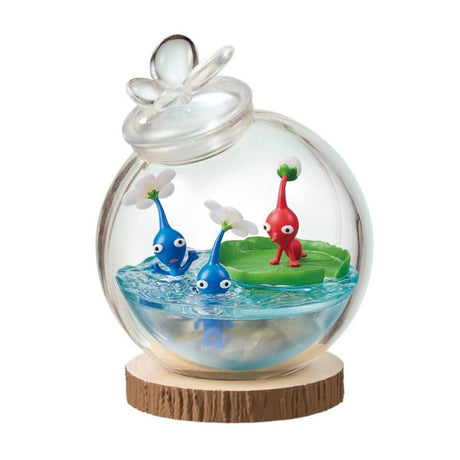 Officially licensed Re-Ment Pikmin Terrarium Collection Figure featuring one Red Pikmin on a giant green water lily pad and two Blue Pikmin in the clear 'water' base. All are enclosed in a round clear glass globe with a water drop design stopper, placed on a wood slice base.
