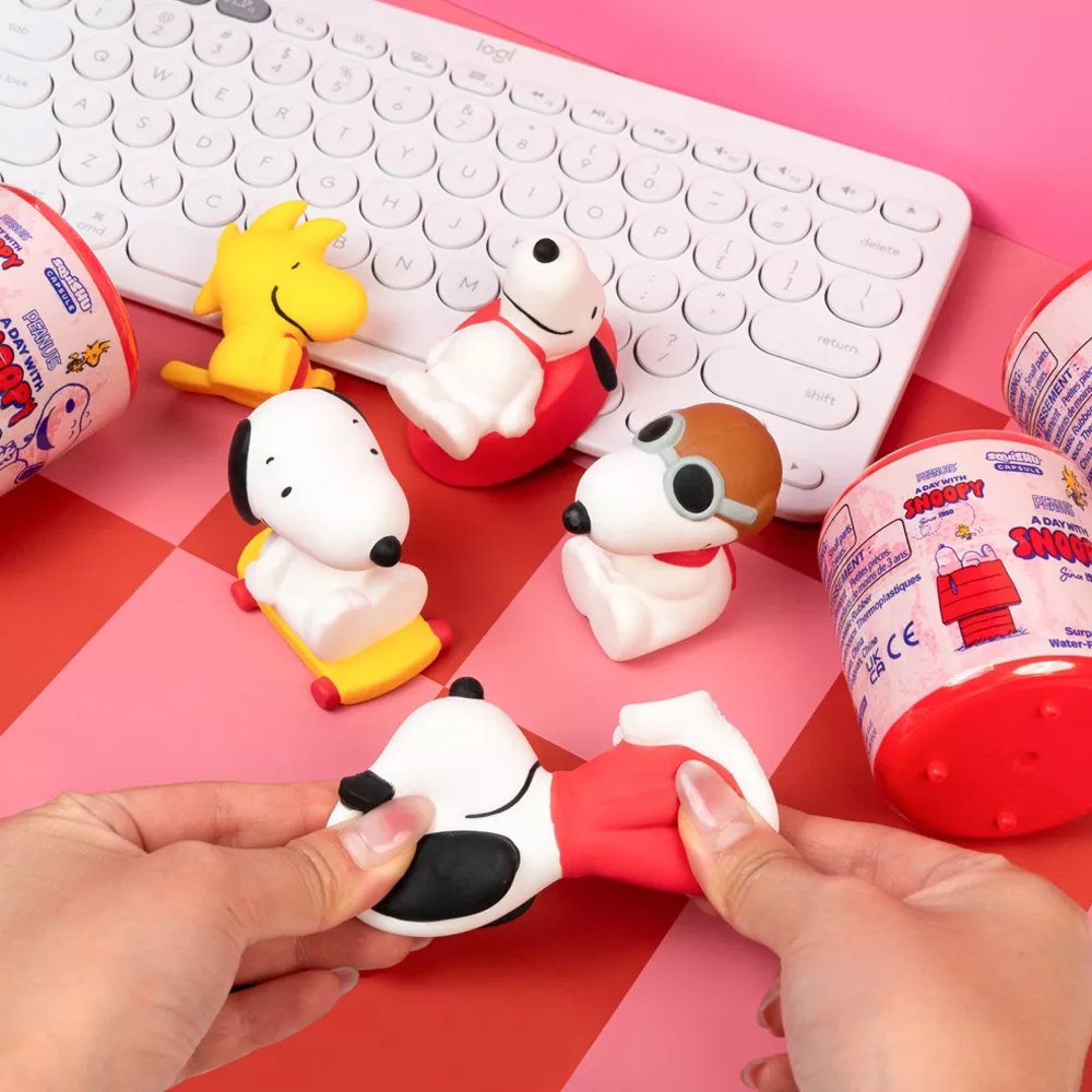 Officially licensed Peanuts Snoopy and Woodstock Squishu water-filled squishy figures in various poses displayed alongside a red surprise capsule