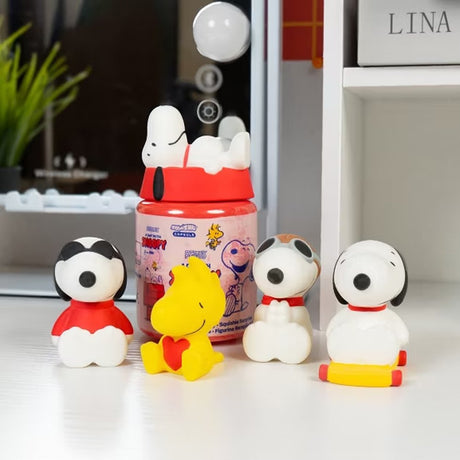 Officially licensed Peanuts Snoopy and Woodstock Squishu water-filled squishy figures in various poses displayed alongside a red surprise capsule