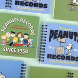 An overhead shot showing multiple officially licensed Peanuts spiral notebooks in green and blue layouts, showcasing the different vintage-inspired cover designs and black spiral bindings.