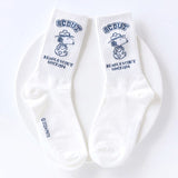 A set of five crew-length socks in black, beige, white, green, and mustard yellow. Each sock features an embroidered graphic of Snoopy as a Beagle Scout leader.