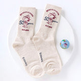 A set of five crew-length socks in black, beige, white, green, and mustard yellow. Each sock features an embroidered graphic of Snoopy as a Beagle Scout leader.