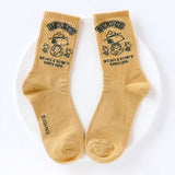 A set of five crew-length socks in black, beige, white, green, and mustard yellow. Each sock features an embroidered graphic of Snoopy as a Beagle Scout leader.