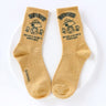 A set of five crew-length socks in black, beige, white, green, and mustard yellow. Each sock features an embroidered graphic of Snoopy as a Beagle Scout leader.