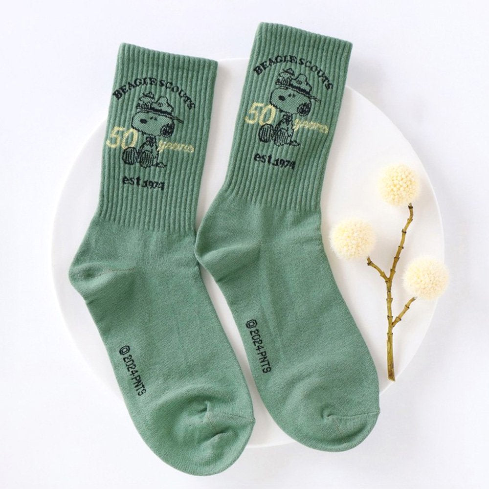 A set of five crew-length socks in black, beige, white, green, and mustard yellow. Each sock features an embroidered graphic of Snoopy as a Beagle Scout leader.