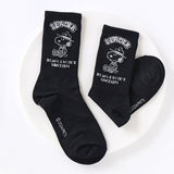 A set of five crew-length socks in black, beige, white, green, and mustard yellow. Each sock features an embroidered graphic of Snoopy as a Beagle Scout leader.