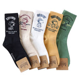A set of five crew-length socks in black, beige, white, green, and mustard yellow. Each sock features an embroidered graphic of Snoopy as a Beagle Scout leader.
