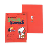 Two officially licensed Peanuts notebooks in red and blue featuring Snoopy and Charlie Brown. The image demonstrates the unique "wing" cover flaps being used as bookmarks and page markers within the lined journal pages.