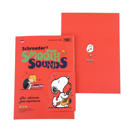 Two officially licensed Peanuts notebooks in red and blue featuring Snoopy and Charlie Brown. The image demonstrates the unique "wing" cover flaps being used as bookmarks and page markers within the lined journal pages.