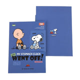 Two officially licensed Peanuts notebooks in red and blue featuring Snoopy and Charlie Brown. The image demonstrates the unique "wing" cover flaps being used as bookmarks and page markers within the lined journal pages.
