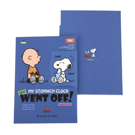 Two officially licensed Peanuts notebooks in red and blue featuring Snoopy and Charlie Brown. The image demonstrates the unique "wing" cover flaps being used as bookmarks and page markers within the lined journal pages.