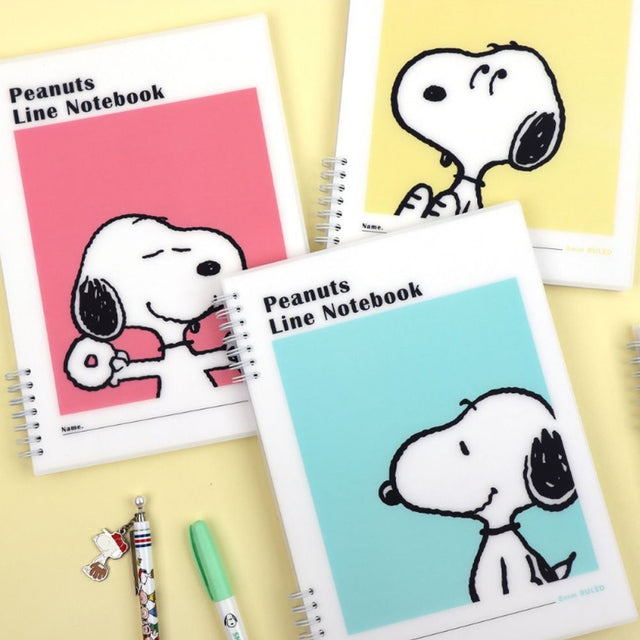 Three officially licensed Peanuts line notebooks with translucent covers in soft hues of pink, yellow, and green, each featuring a large illustration of Snoopy. The interior view shows 8mm ruled pages with small Snoopy graphics at the top and bottom corners.
