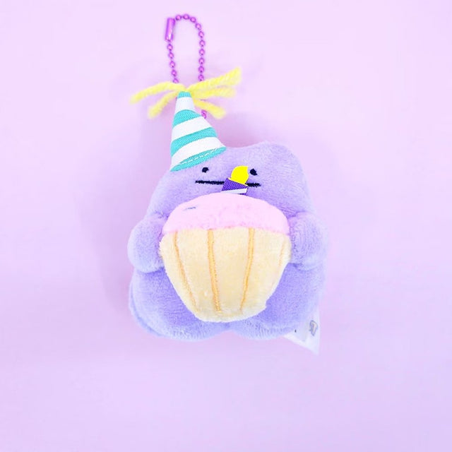 A Pokémon Ditto plush keychain holding a celebration cupcake and wearing a striped party hat with yellow yarn on top, attached to a colorful ball chain
