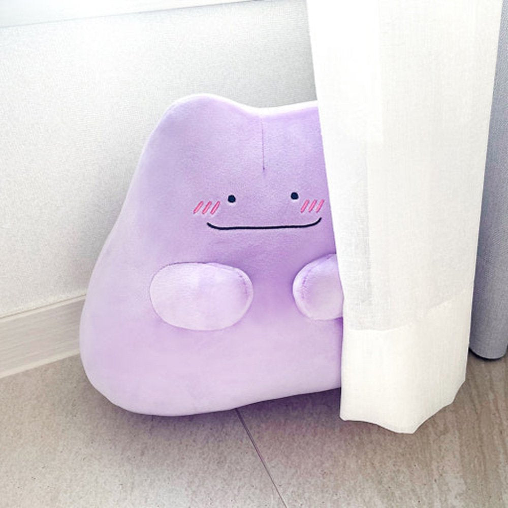 An officially licensed Pokémon Ditto plush toy in a vibrant light purple color. The plush features a simple smile, and three pink diagonal lines on each cheek to represent blushing.