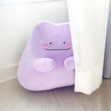 An officially licensed Pokémon Ditto plush toy in a vibrant light purple color. The plush features a simple smile, and three pink diagonal lines on each cheek to represent blushing.