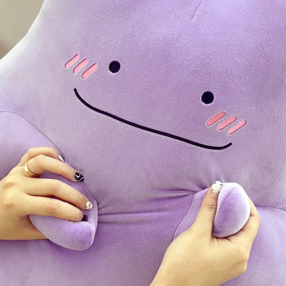 An officially licensed Pokémon Ditto plush toy in a vibrant light purple color. The plush features a simple smile, and three pink diagonal lines on each cheek to represent blushing.