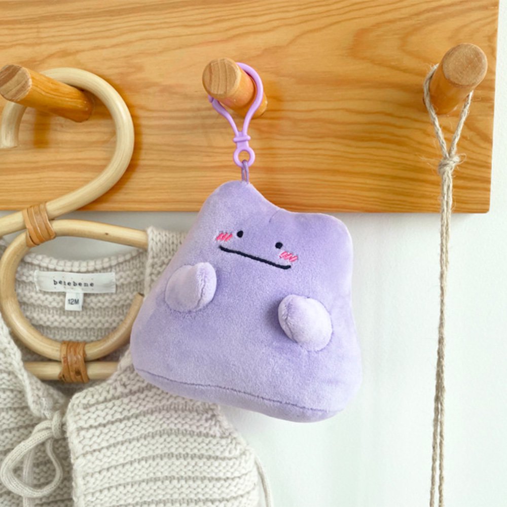 An officially licensed Pokémon Ditto plush clip-on keychain in a vibrant light purple color. The plush features a simple smile, and three pink diagonal lines on each cheek to represent blushing.