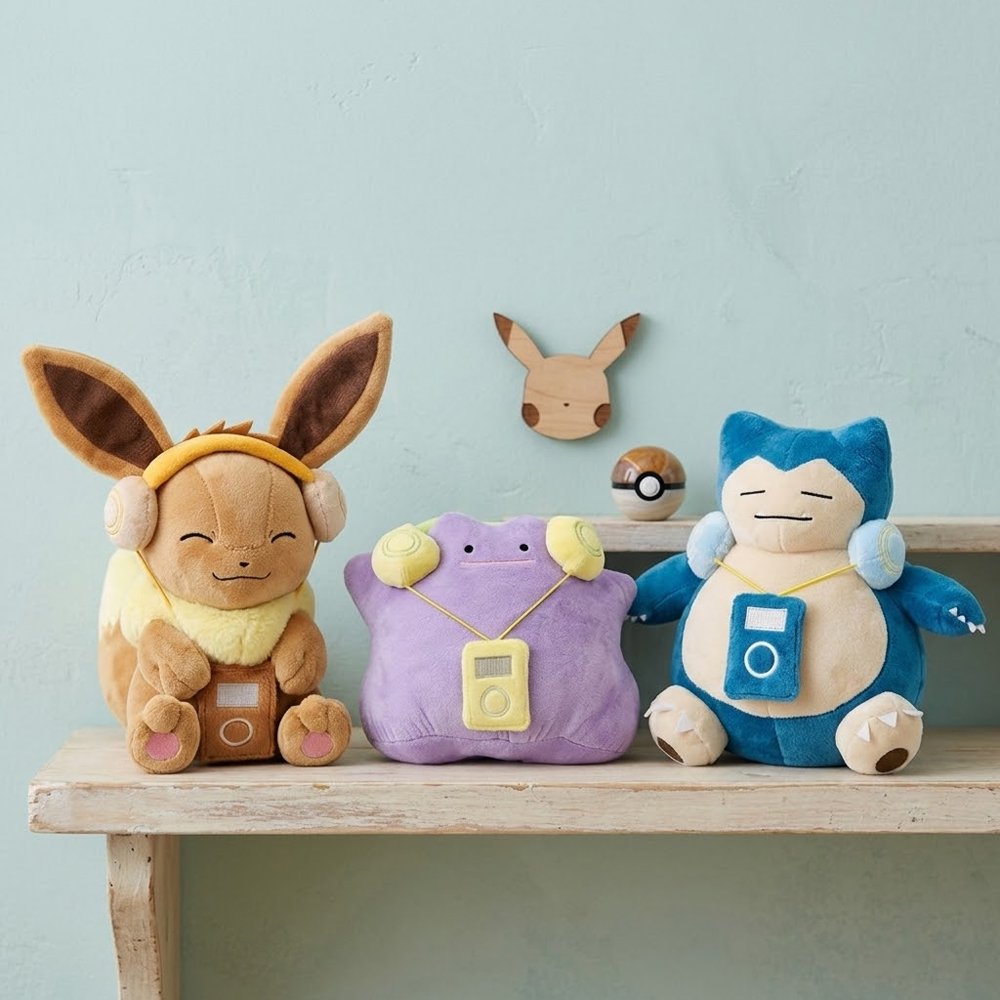 A collection of three officially licensed Pokemon plush toys—Eevee, Ditto, and Snorlax—each sitting upright and vibing out to their favorite tunes with adorable plush headsets and music players