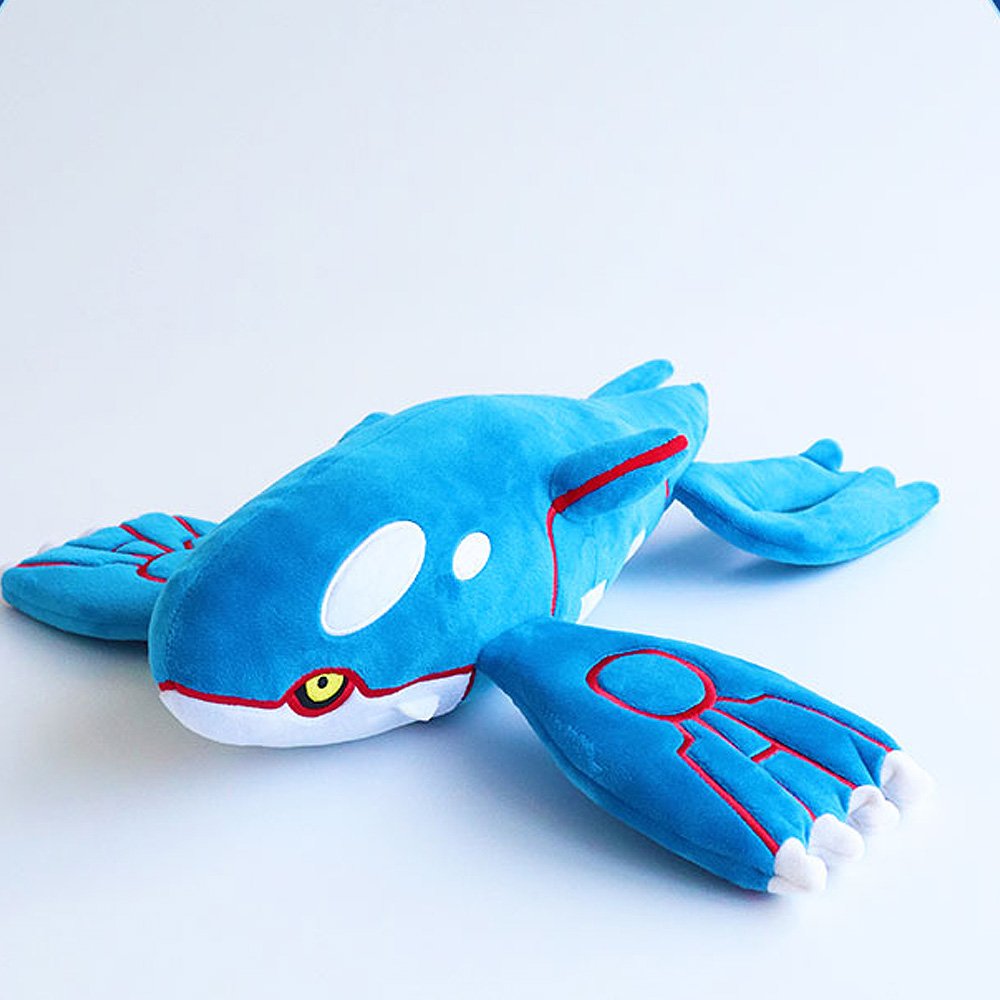 A large, horizontal plush of the Legendary Pokémon Kyogre. The plush is vibrant blue with white oval patches on its head and large, flat flippers featuring red circular patterns and white finger-like tips. It has small yellow eyes and a sleek, aerodynamic body shape.