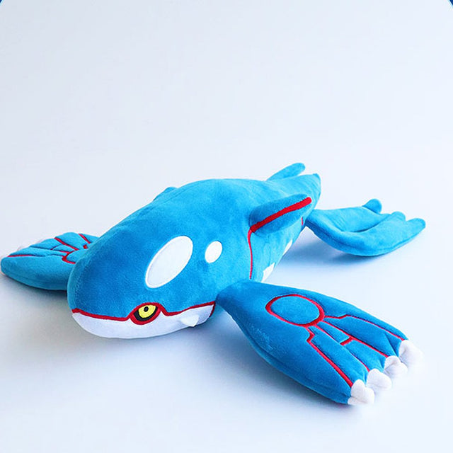 A large, horizontal plush of the Legendary Pokémon Kyogre. The plush is vibrant blue with white oval patches on its head and large, flat flippers featuring red circular patterns and white finger-like tips. It has small yellow eyes and a sleek, aerodynamic body shape.