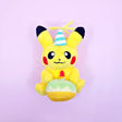 A Pokémon Pikachu plush keychain holding a celebration cupcake and wearing a striped party hat with yellow yarn on top, attached to a colorful ball chain