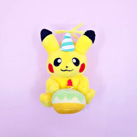 A Pokémon Pikachu plush keychain holding a celebration cupcake and wearing a striped party hat with yellow yarn on top, attached to a colorful ball chain