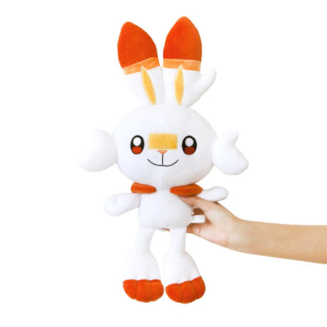 An officially licensed Pokemon plush toy of the Fire-type starter Scorbunny, featuring long ears with orange tips, large embroidered eyes, a yellow bandage-like marking on its nose, and bright orange feet.