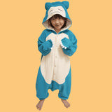 Official Pokémon Snorlax Kids Costume Kigurumi Onesie Jumpsuit worn by a young model. Features a soft teal-blue and cream fleece body, paw sleeves with white claws, and a sleeping Snorlax face hood. Perfect for kids' Halloween costumes, sleepover party pajamas, and holiday gifts