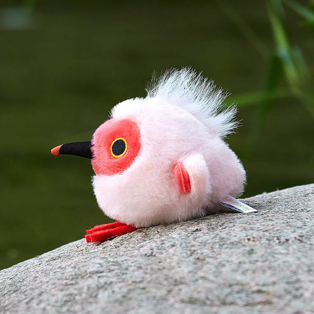 A round, light pink Crested Ibis bird plush keychain with a bright red face, red feet, and a wispy white crest