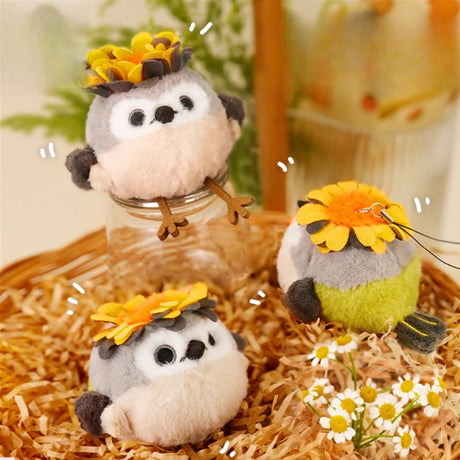 A round, fluffy Goldcrest bird plush keychain with a grey head, cream-colored body, and dark grey wings, wearing a bright yellow head crest, featuring small black eyes and long brown legs