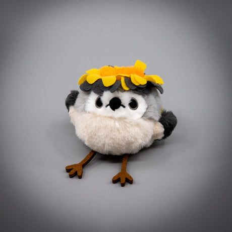 A round, fluffy Goldcrest bird plush keychain with a grey head, cream-colored body, and dark grey wings, wearing a bright yellow head crest, featuring small black eyes and long brown legs