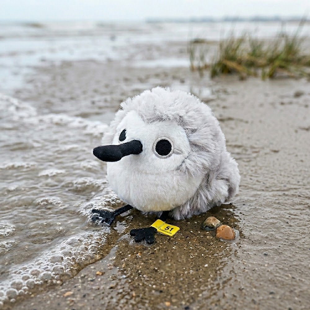 A round, fluffy white and grey Sandpiper bird plush keychain with a black spoon-shaped beak and small black feet