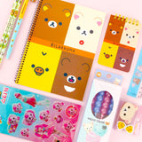 Two officially licensed Rilakkuma and Chairoikoguma stationery sets in clear plastic carry cases with handles. Both cases are packed with notebooks, pencils, and other stationery items.