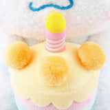 Officially licensed Sanrio Cinnamoroll plush, wearing a charming white party hat topped with a bright yellow tassel, and holding a cake for celebrating a special day.