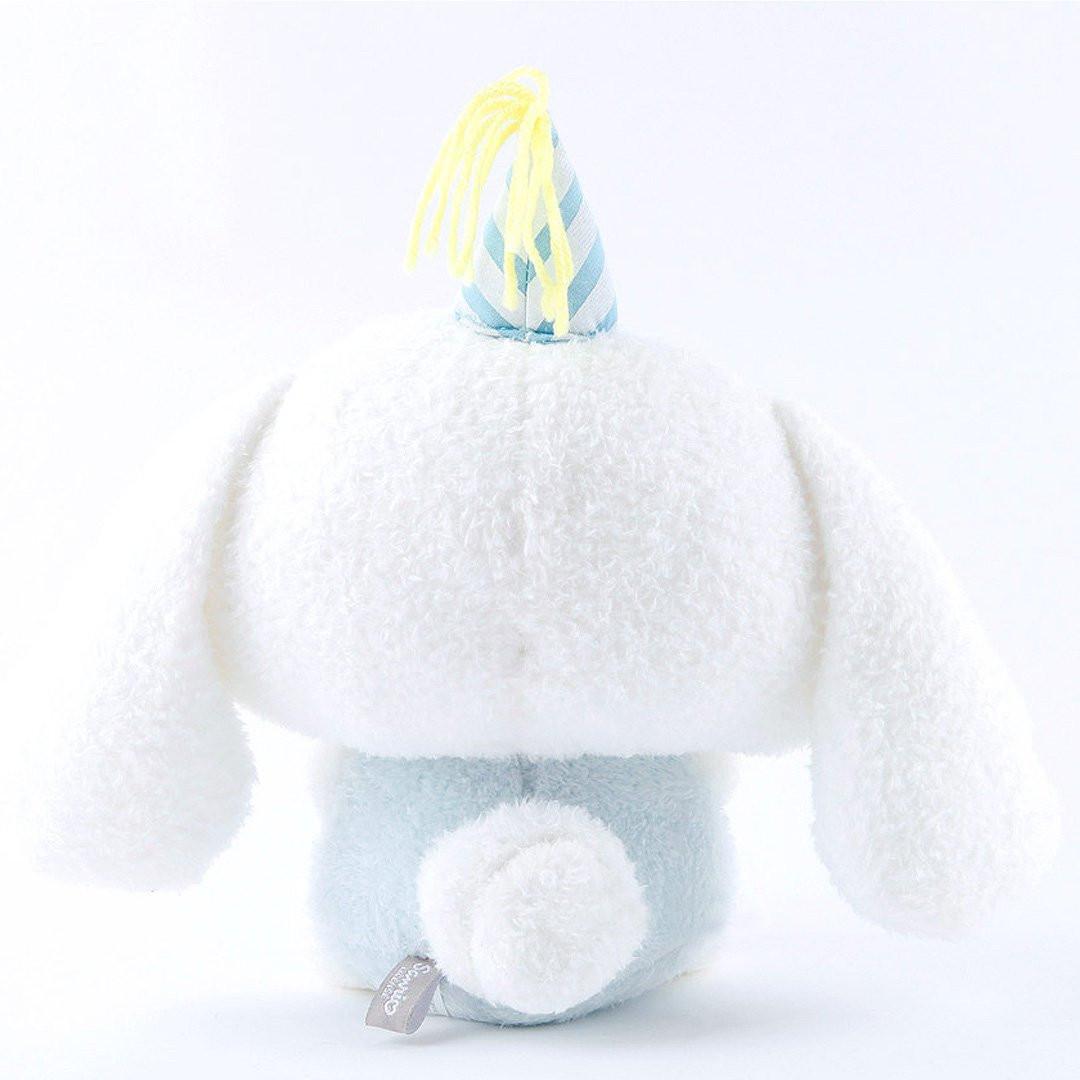 Officially licensed Sanrio Cinnamoroll plush, wearing a charming white party hat topped with a bright yellow tassel, and holding a cake for celebrating a special day.