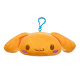 An officially licensed Sanrio plush keychain of Cinnamoroll in a golden-brown bread-like color. The plush features his long ears, purple blushing cheeks, and a blue plastic attachment clip.