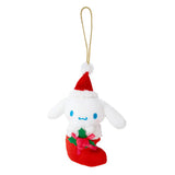 Sanrio Cinnamoroll is dressed for the season wearing a red Santa hat with a white pom-pom while sporting his signature red bow. He sits snugly in a red Christmas stocking adorned with green holly leaves and a decorative ribbon. Crafted from soft plush material, this ornament has a cozy, huggable feel. The attached gold cord loop makes it easy to hang on your Christmas tree.