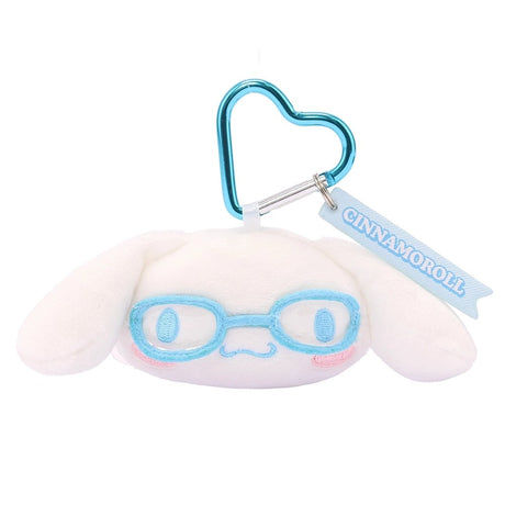 An officially licensed Sanrio Cinnamoroll plush head keychain, wearing embroidered sky blue glasses. The keychain features a sky blue, heart-shaped metal carabiner clip and a woven fabric tag that reads "CINNAMOROLL." The sturdy, heart-shaped carabiner in a matching metallic sky blue finish, makes it easy to clip onto backpacks, purses, or belt loops.