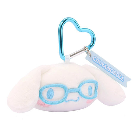 An officially licensed Sanrio Cinnamoroll plush head keychain, wearing embroidered sky blue glasses. The keychain features a sky blue, heart-shaped metal carabiner clip and a woven fabric tag that reads "CINNAMOROLL." The sturdy, heart-shaped carabiner in a matching metallic sky blue finish, makes it easy to clip onto backpacks, purses, or belt loops.