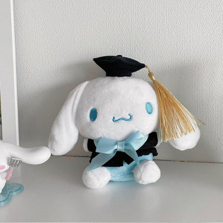 An officially licensed Sanrio Cinnamoroll plush toy dressed in a black graduation cap with a gold tassel and a matching gown featuring a large light blue bow