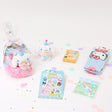 A collection of Sanrio Cinnamoroll Happy Birthday themed gift sets, each containing various colorful items such as plush keychains and socks, all packaged in clear gift bags with pink ribbons.